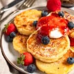syrniki on a plate topped with yogurt, powdered sugar, and fresh berries.