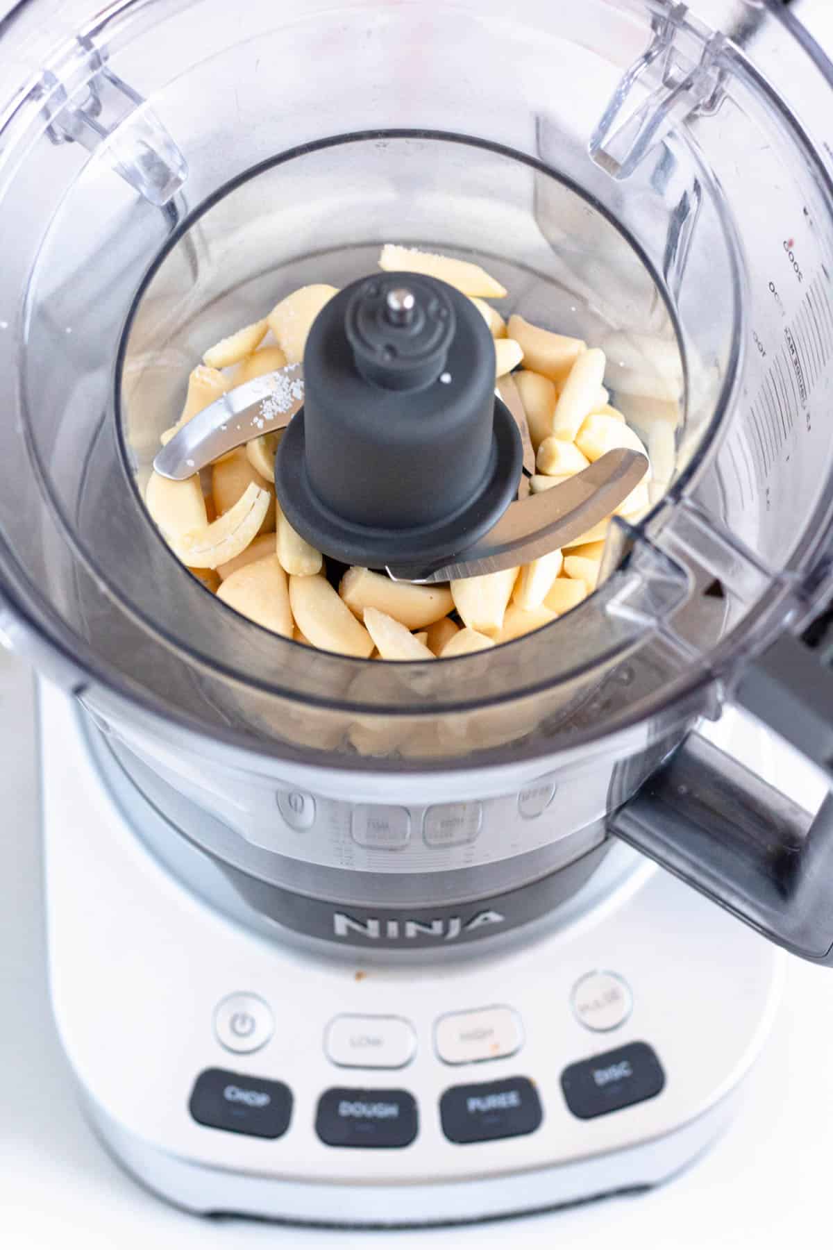 Garlic cloves and kosher salt added to a food processor. 