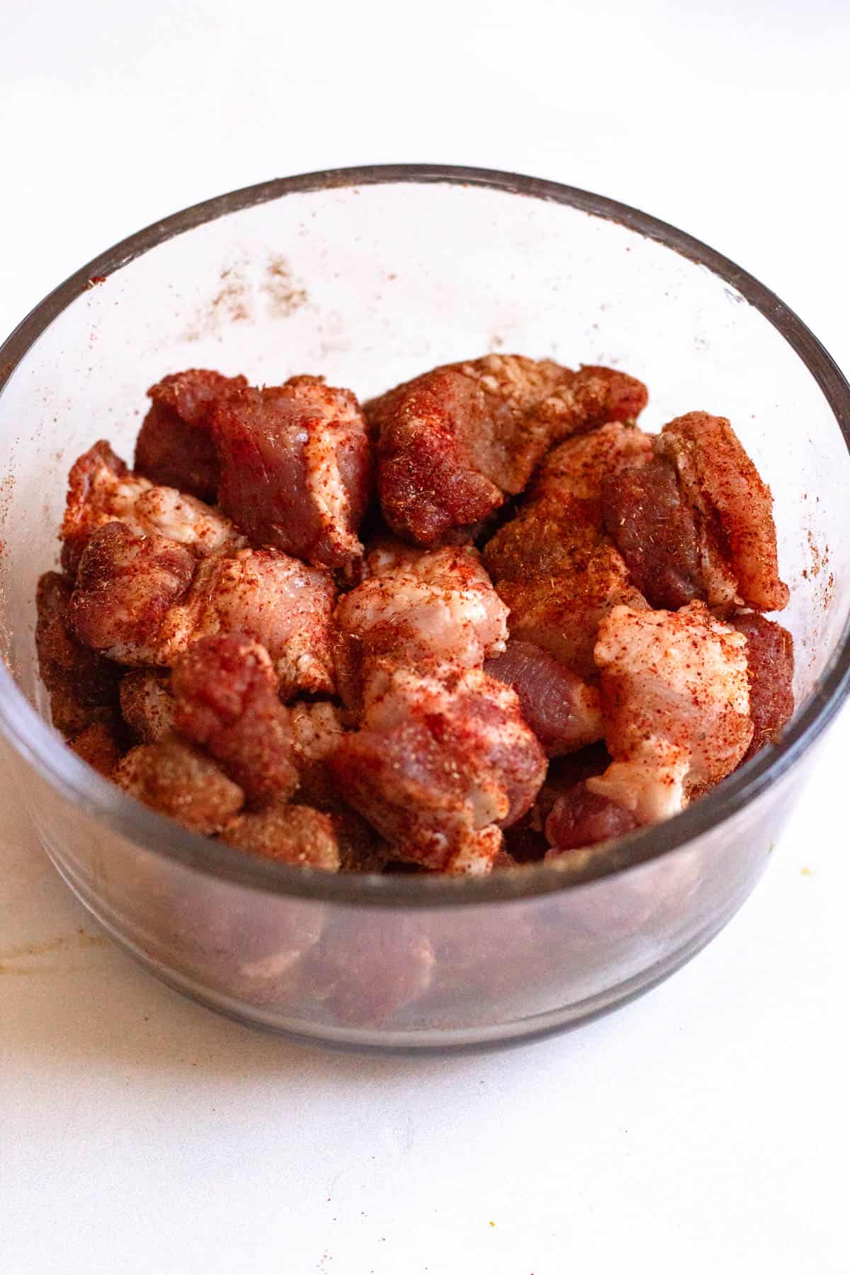Pork belly combined with a mixture of seasonings in a glass bowl. 