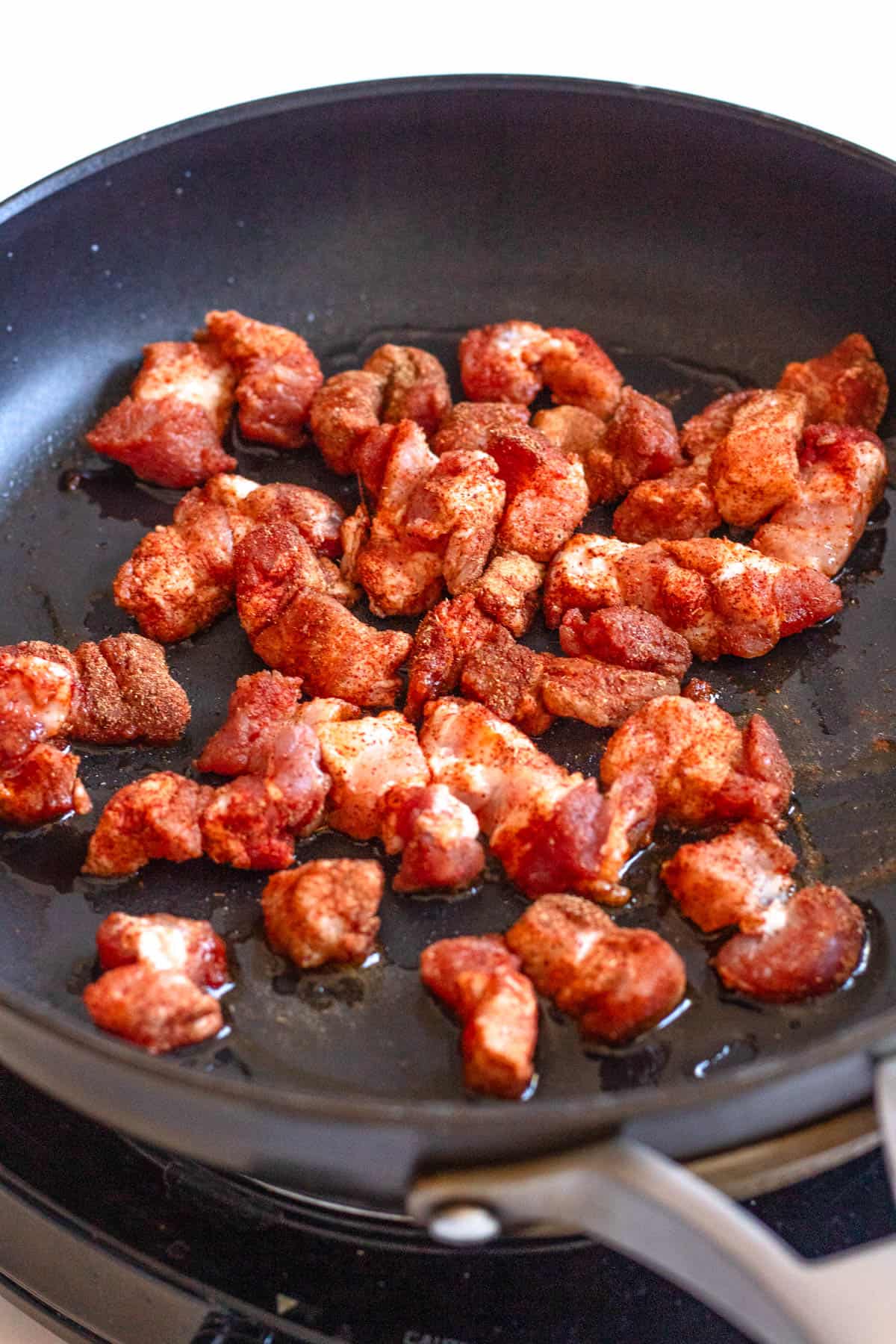 Seasoned pork belly frying in a skillet. 