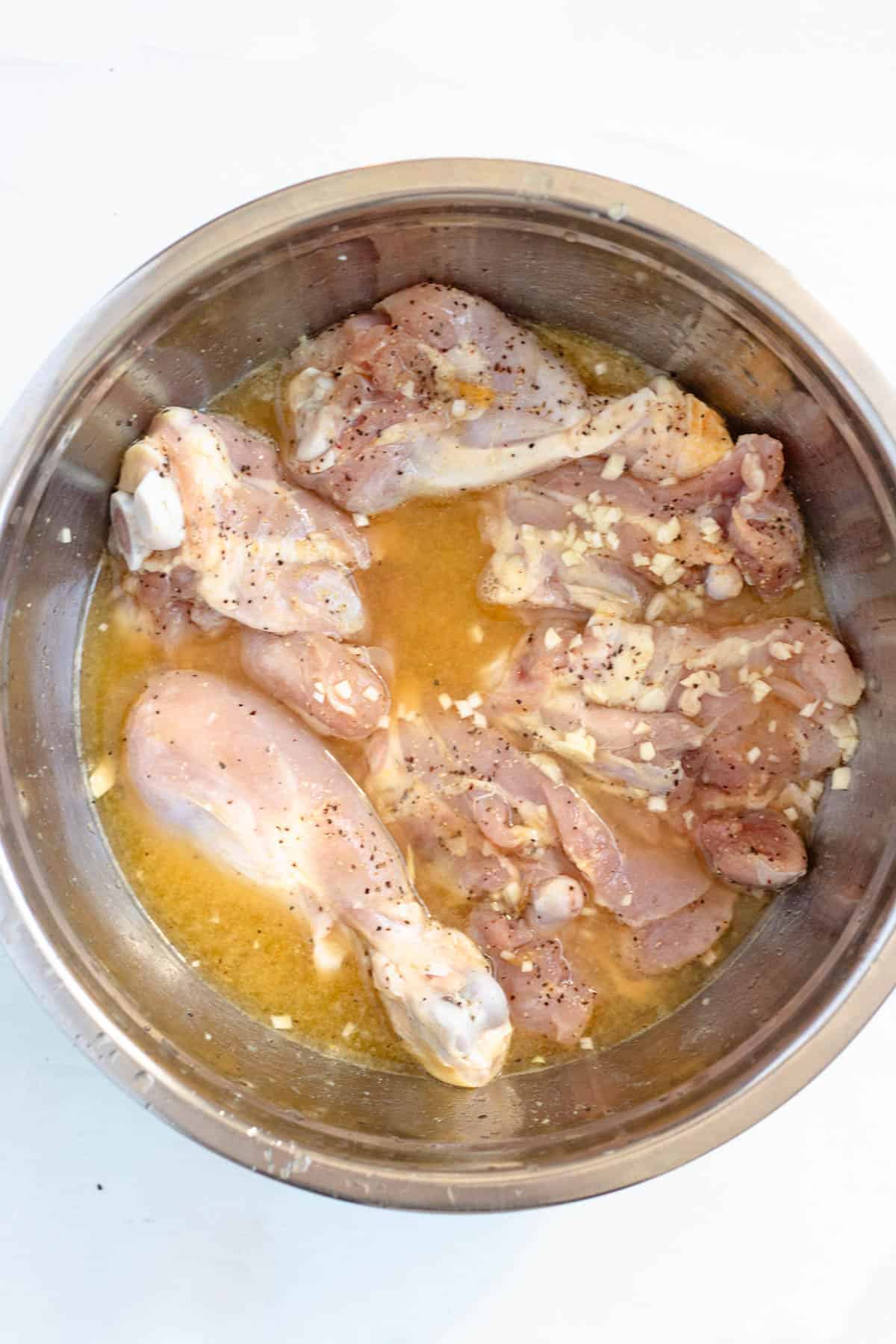 Raw chicken marinating in orange and lime juice in a large mixing bowl. 