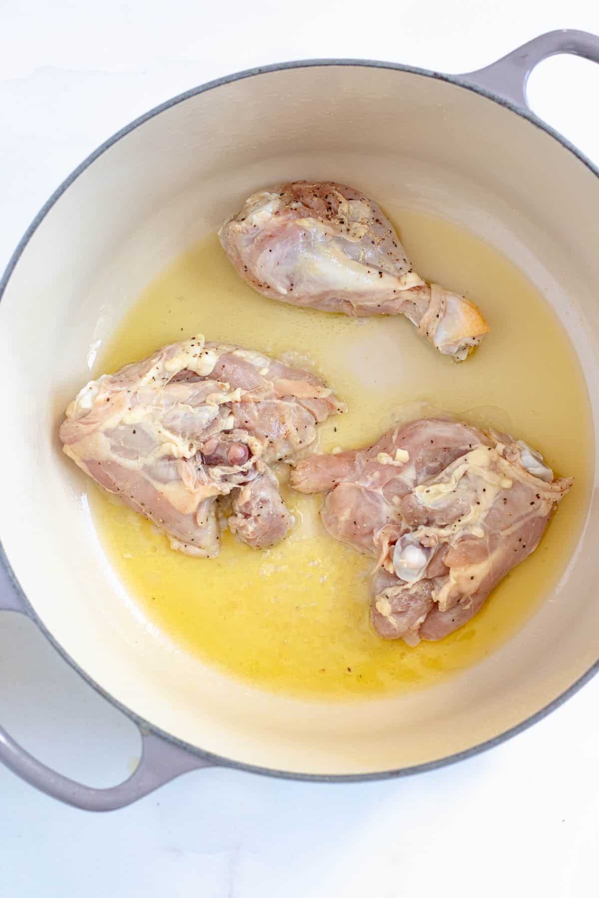 Chicken being braised in a Dutch oven with oil for fricase de pollo. 