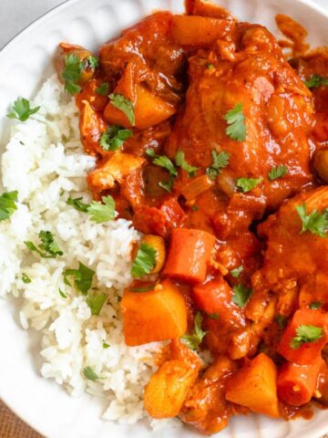 Fricase de Pollo, a hearty Cuban stew, served over white rice on a plate and garnished with chopped cilantro.