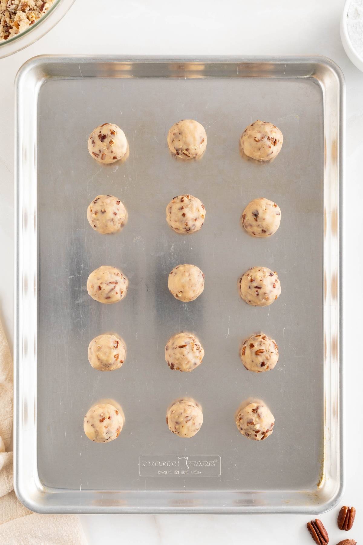 Pecan snowball cookie dough rolled into balls and placed on a baking sheet to bake. 
