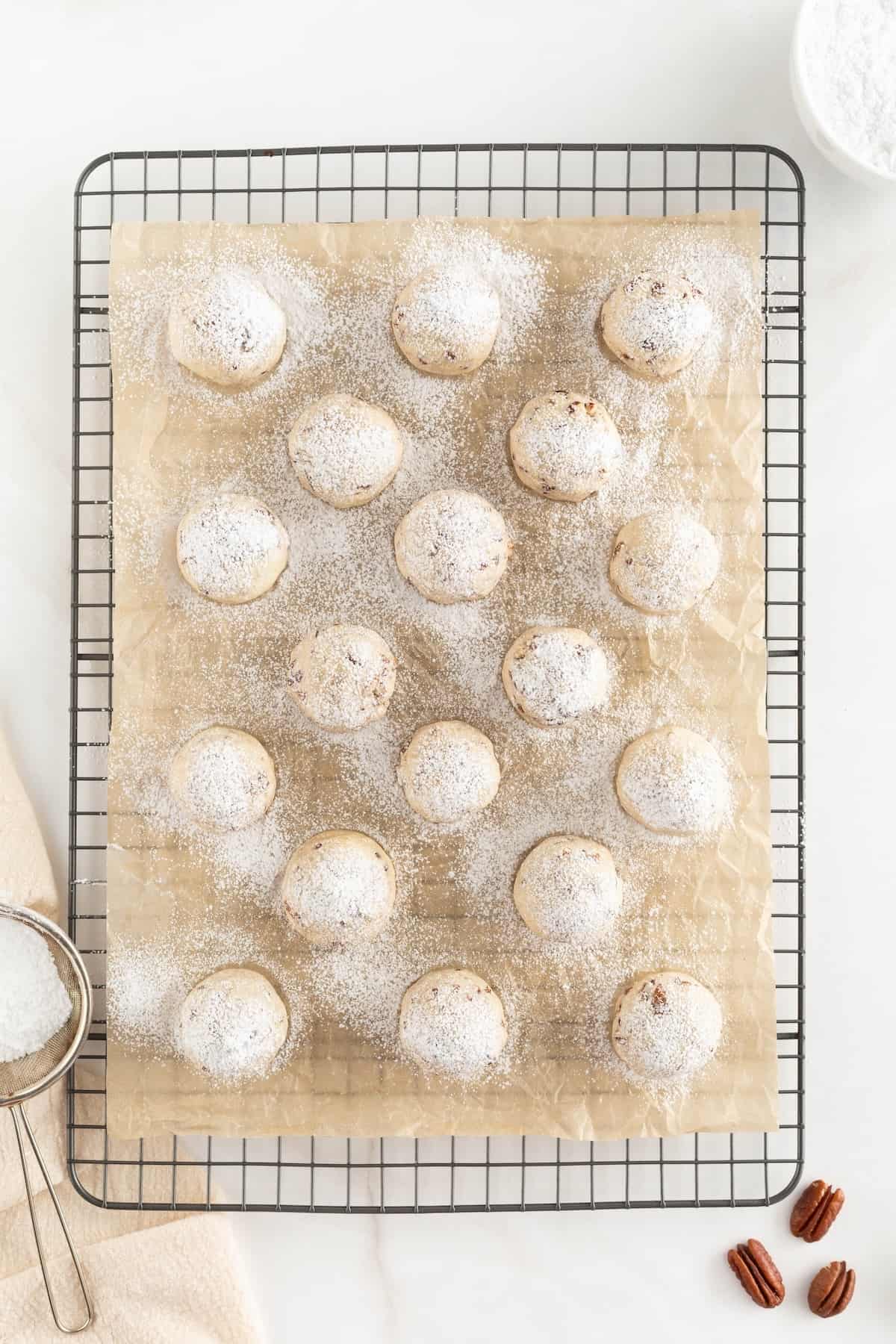 Baked buttery pecan snowball cookies on parchment paper with powdered sugar sprinkled over top. 