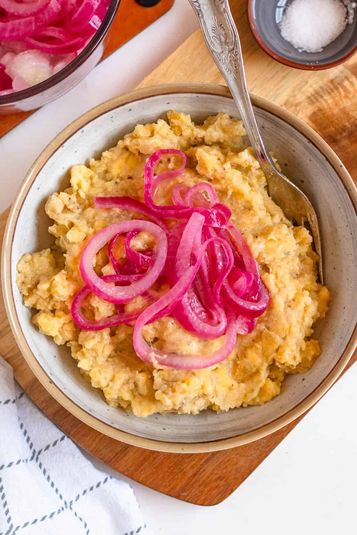 A fork resting in a bowl of mangu breakfast with red onions garnished on top. 