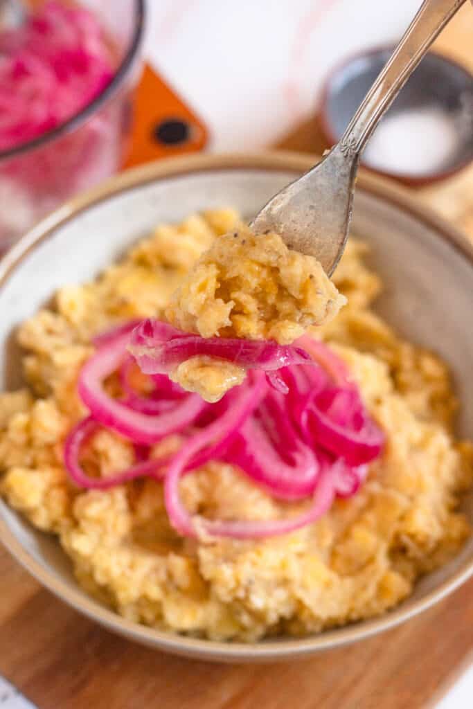 A forkful of mangu with red onions coming out of the bowl. 