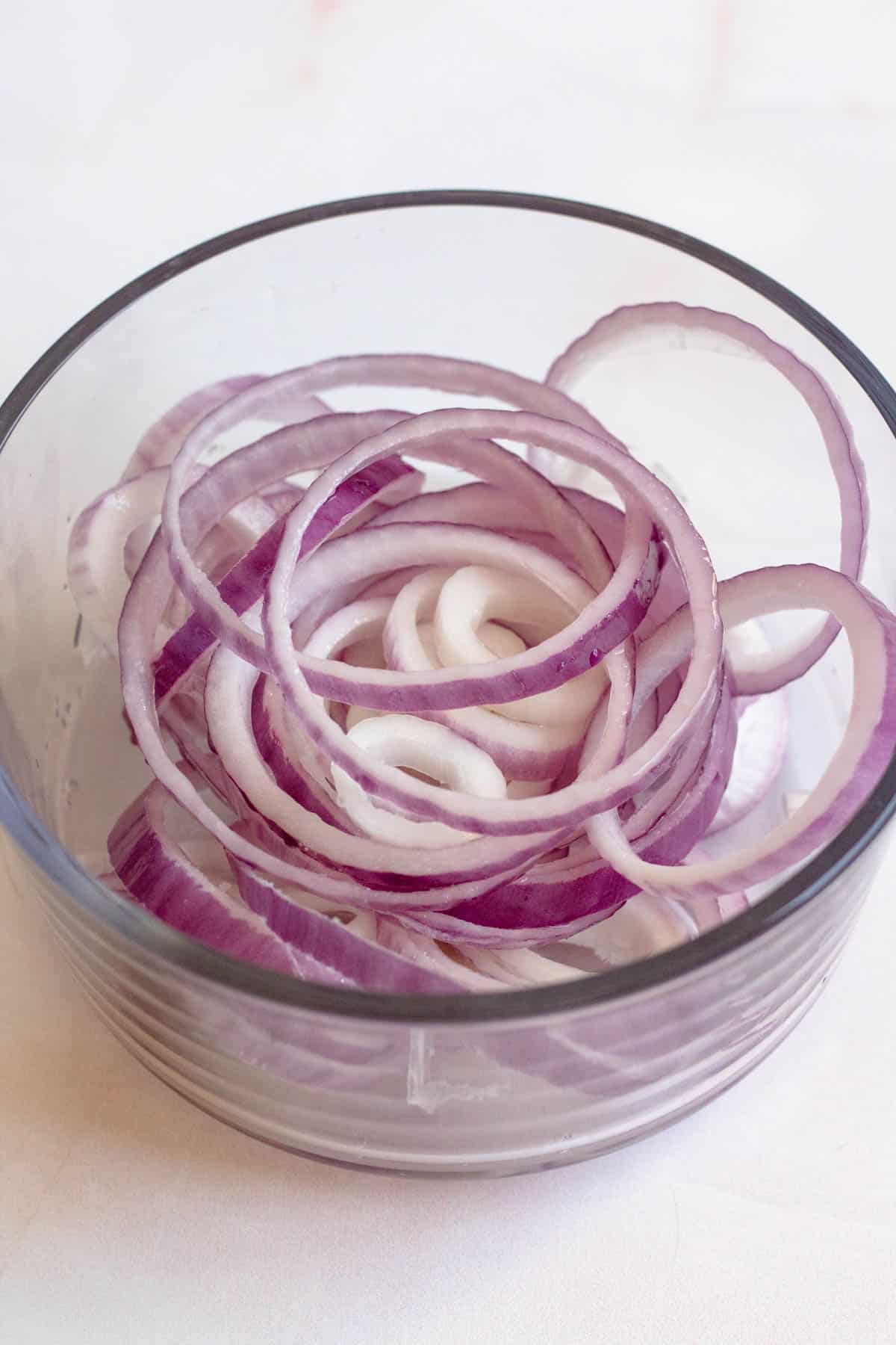 Sliced red onions and white vinegar in a bowl for mangu recipe. 
