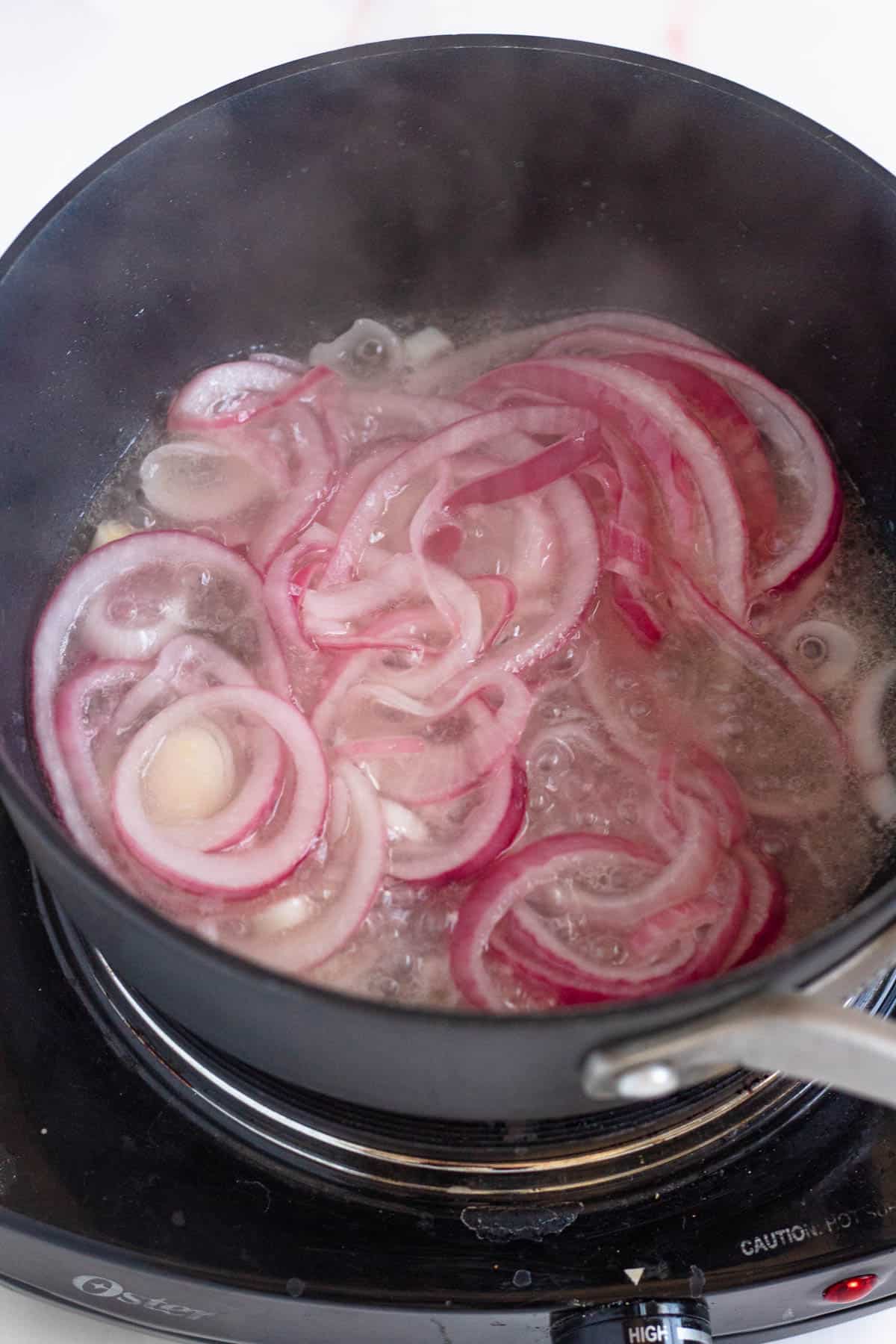 Red onions boiling in a saucepan to prepare for a mangu breakfast. 