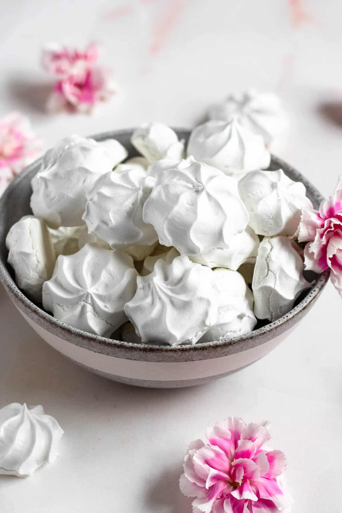 Bowl of white suspiros in a bowl with pink and white flowers on the side of the bowl. 