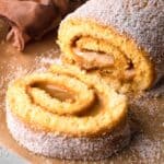 A Brazo de Reina cake rolled up on a piece of parchment paper with a linen in the background