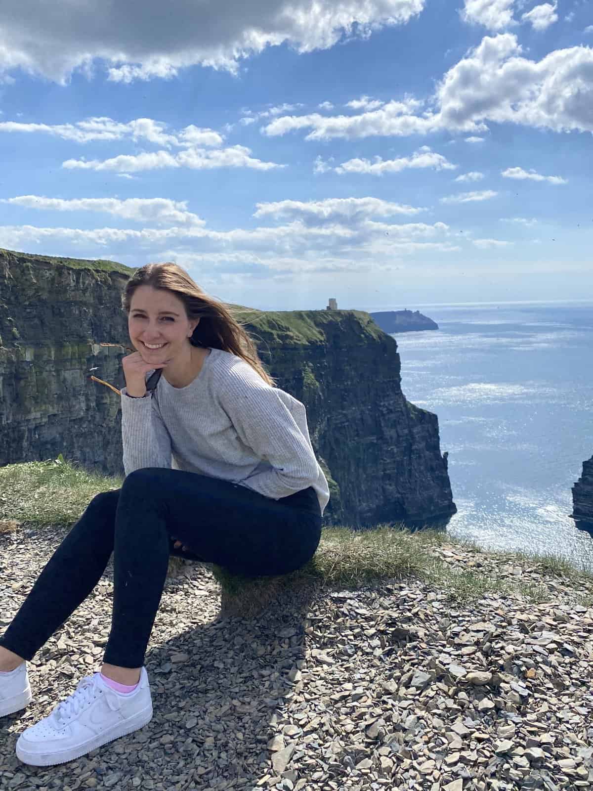 A girl posing in front of the Cliffs of Moher in Ireland.