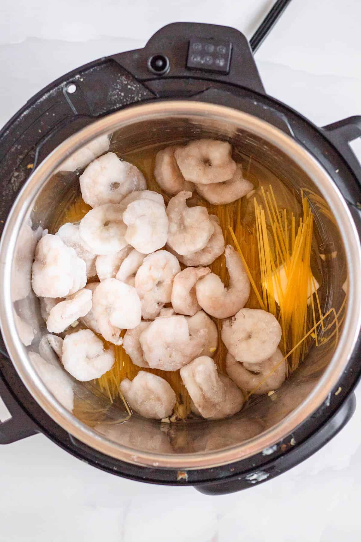 Shrimp Scampi ingredients, including frozen shrimp and uncooked angel hair pasta, in the bowl of an instant pot.
