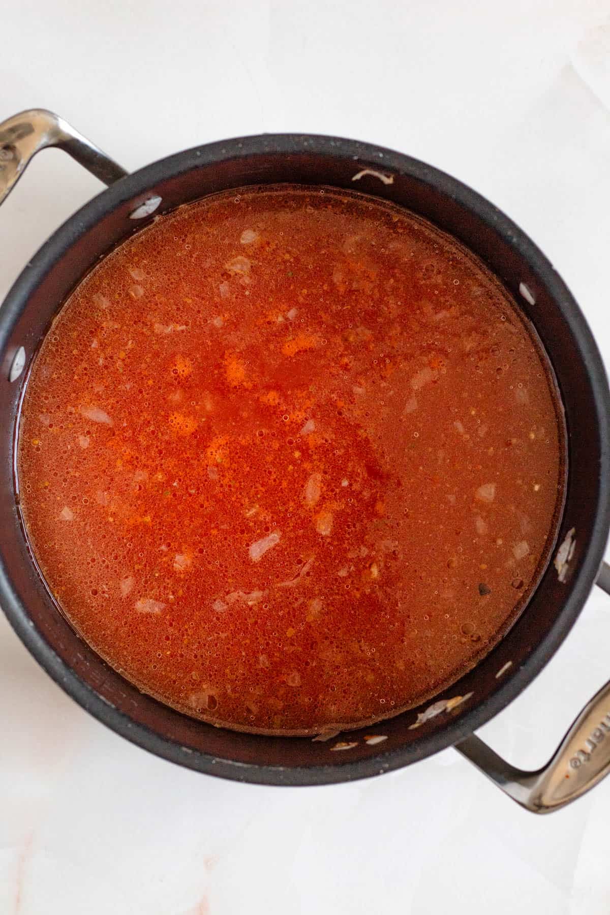 a large black pot with tomato sauce and chicken broth added.