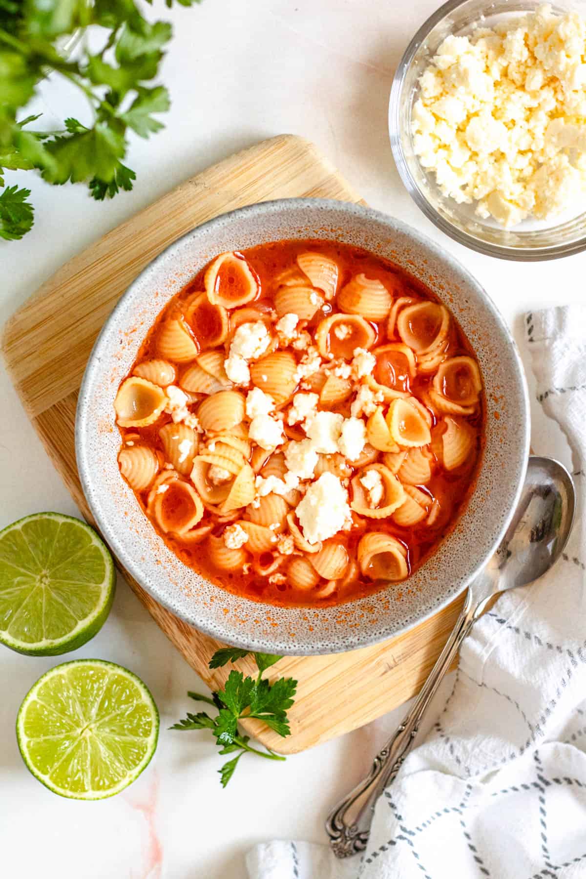 a bowl of sopita topped with queso fresco and next to half of a lime.