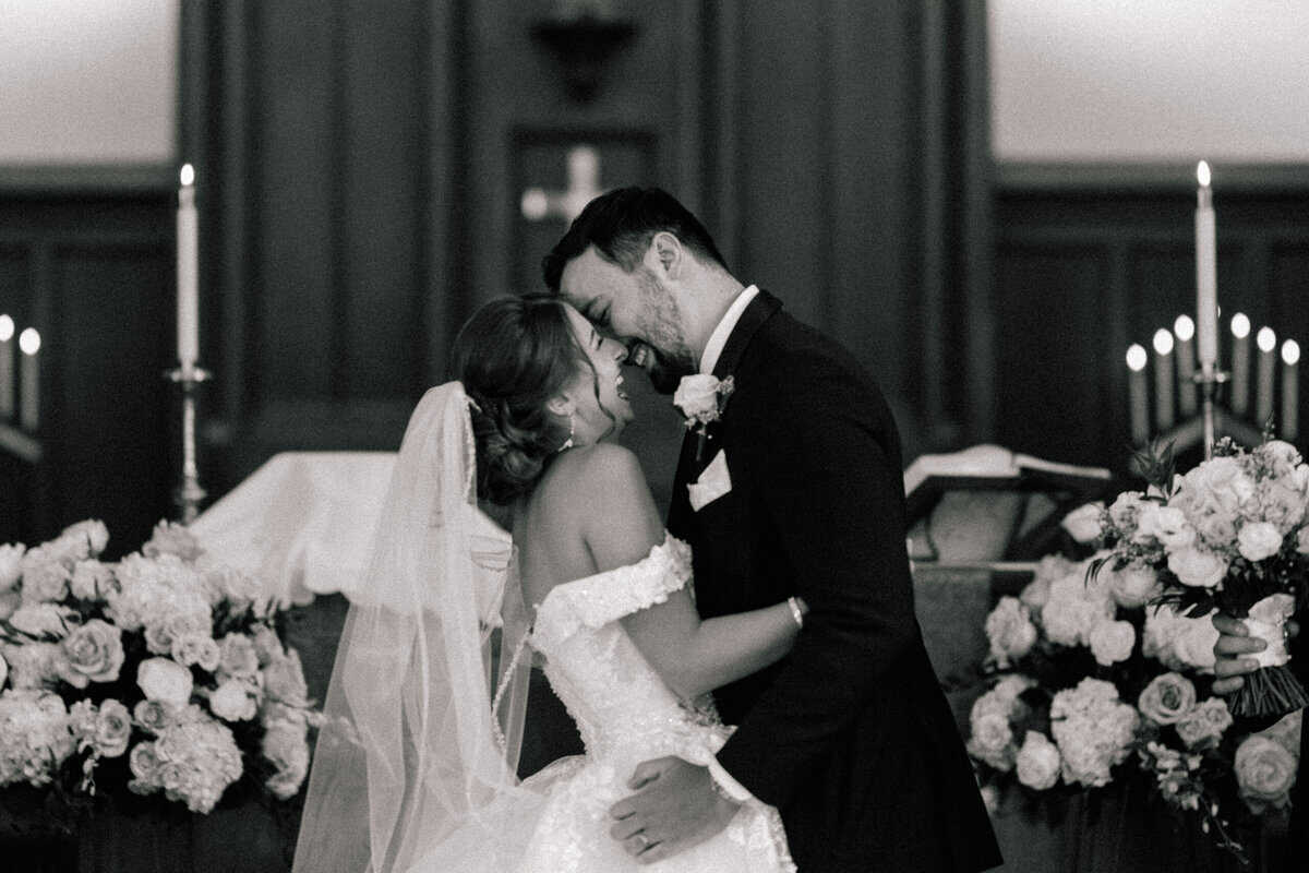A bride and groom kissing on the altar. 