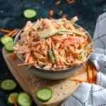 Kani Salad in a large bowl surrounded by carrots, cucumbers, and a linen.