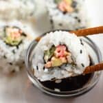 chopsticks dipping a piece of Kani Sushi into soy sauce.