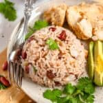 Belizean Rice and Beans in a pile on a plate surrounded by avocado and cilantro.