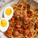 Pinterest image of a plate of Haitian Spaghetti with a boiled egg, halved, garnished on the side.