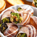 Pinterest image of a close-up shot of a bowl of Escargot with seasonings added to a snail shell.