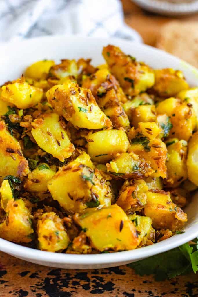 Close-up picture of Jeera Aloo, spiced potatoes with cumin, turmeric, and fresh coriander, served in a white bowl.