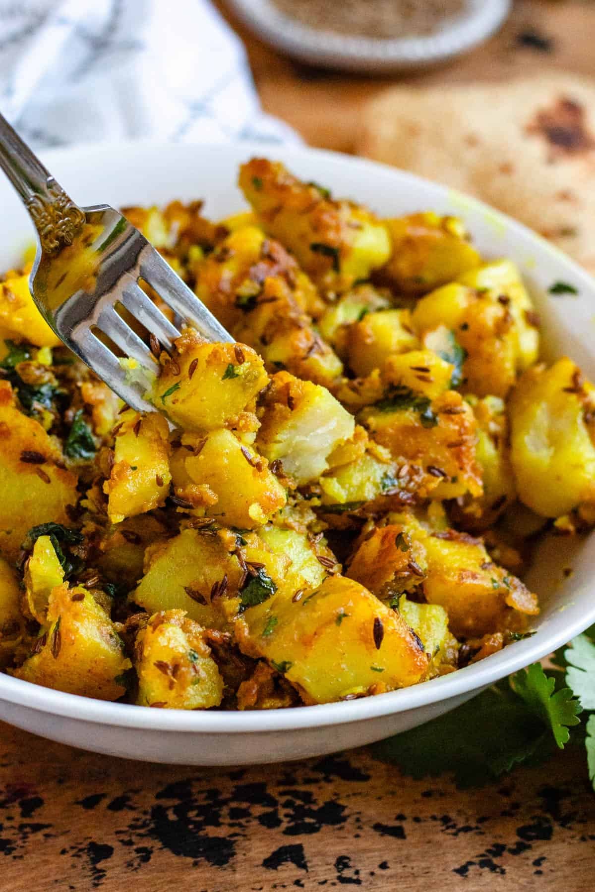 Jeera Aloo served in a white bowl, with a fork.