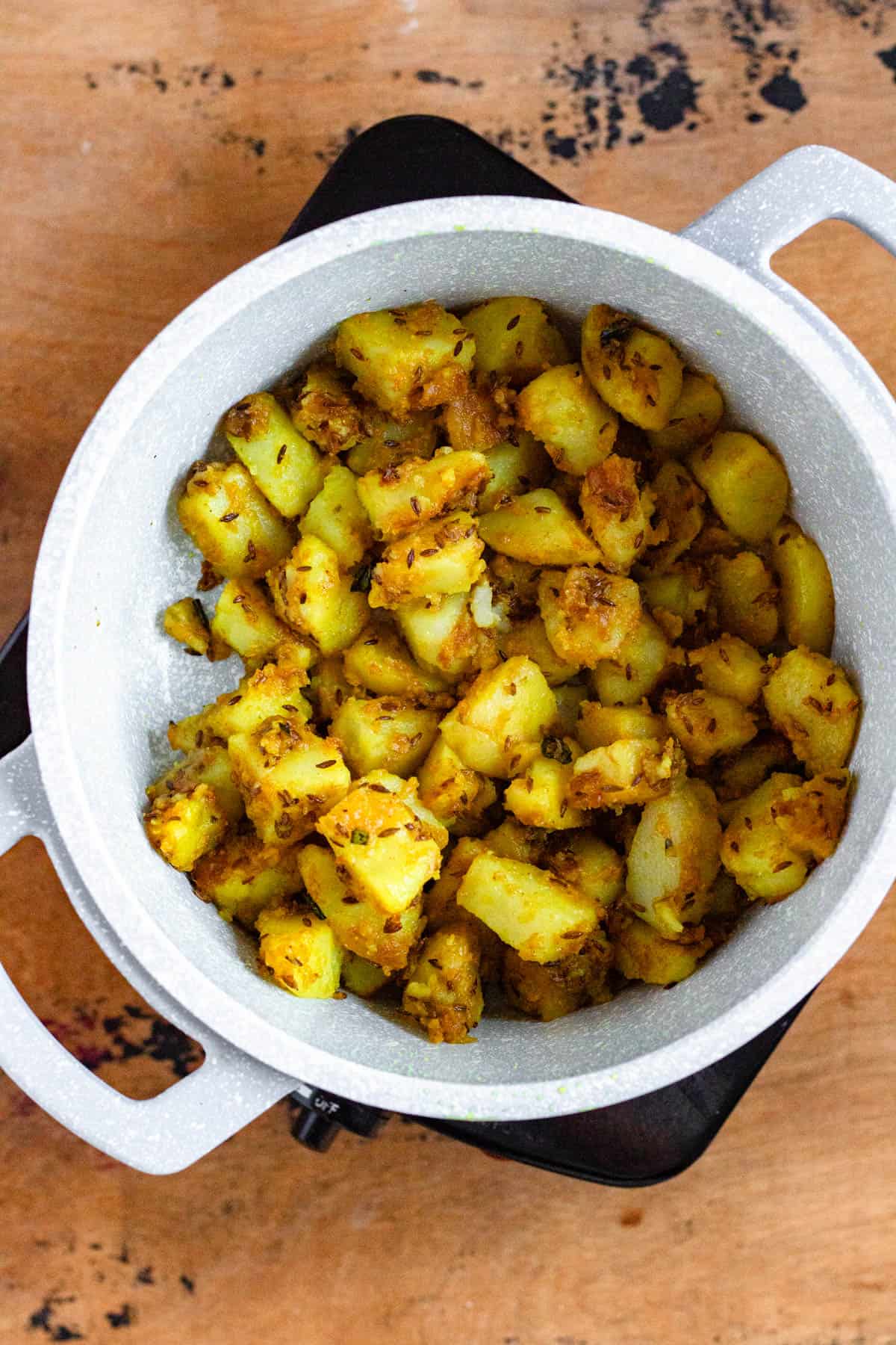 Spiced potatoes with cumin seeds in a white pot on a stovetop.