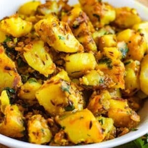Close-up picture of Jeera Aloo, spiced potatoes with cumin, turmeric, and fresh coriander, served in a white bowl.