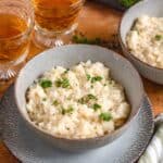 A bowl of creamy parmesan risotto with parsley on top and wine behind.