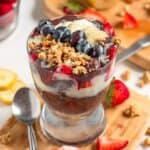 A refreshing Açaí Na Tigela layered with granola, sliced bananas, strawberries, blueberries, and a drizzle of creamy topping.