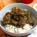 A bowl of rich cassava leaf served over rice, with habanero peppers on the side.