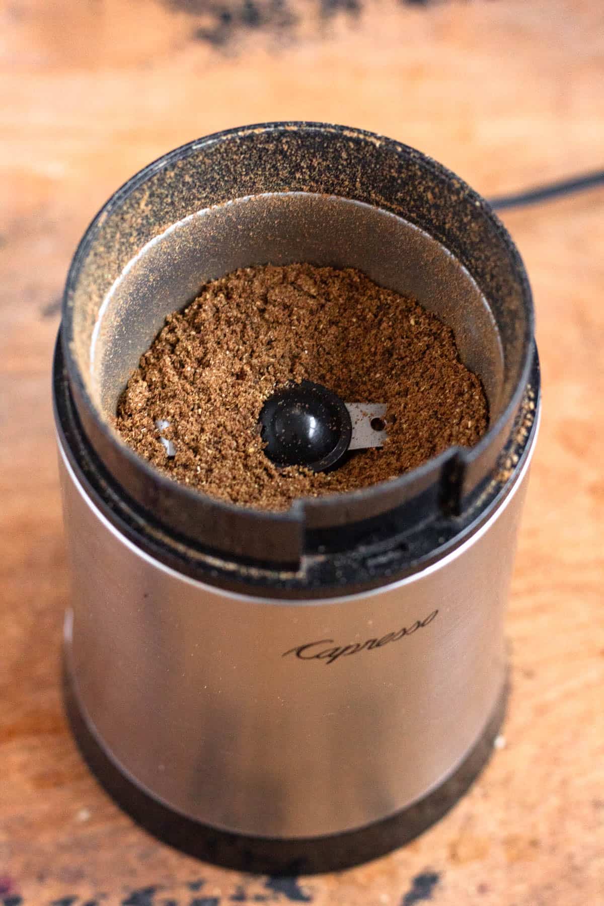 Roasted cinnamon sticks, cloves, cumin, cardamom, and coriander are ground together in a spice grinder.