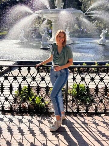 Photo of a girl in front of a fountain holding a coffee and wearing jeans
