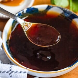 A spoonful of dark 3 ingredient stir fry sauce held over a bowl of the same sauce.
