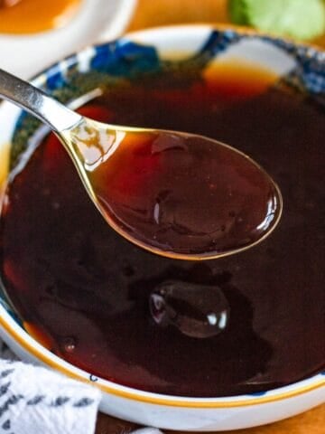 A spoonful of dark 3 ingredient stir fry sauce held over a bowl of the same sauce.