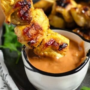 A close-up of chicken satay being dipped into a small bowl of creamy peanut sauce.