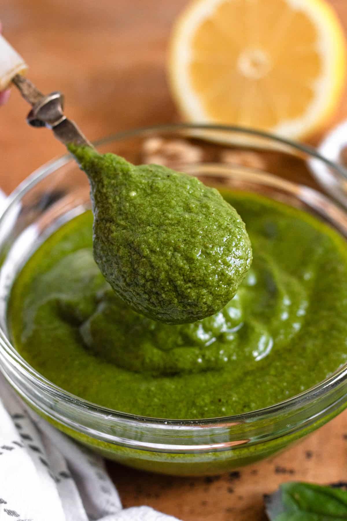 A spoonful of green walnut pesto in a glass bowl, with a halved lemon in the background.