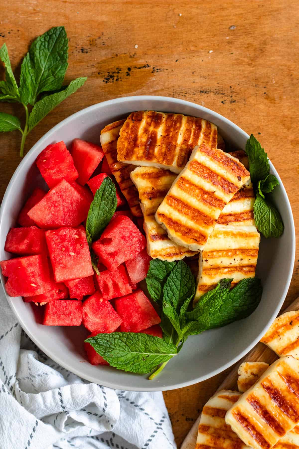A top view image of grilled halloumi slices served with fresh watermelon cubes and mint leaves in a bowl.