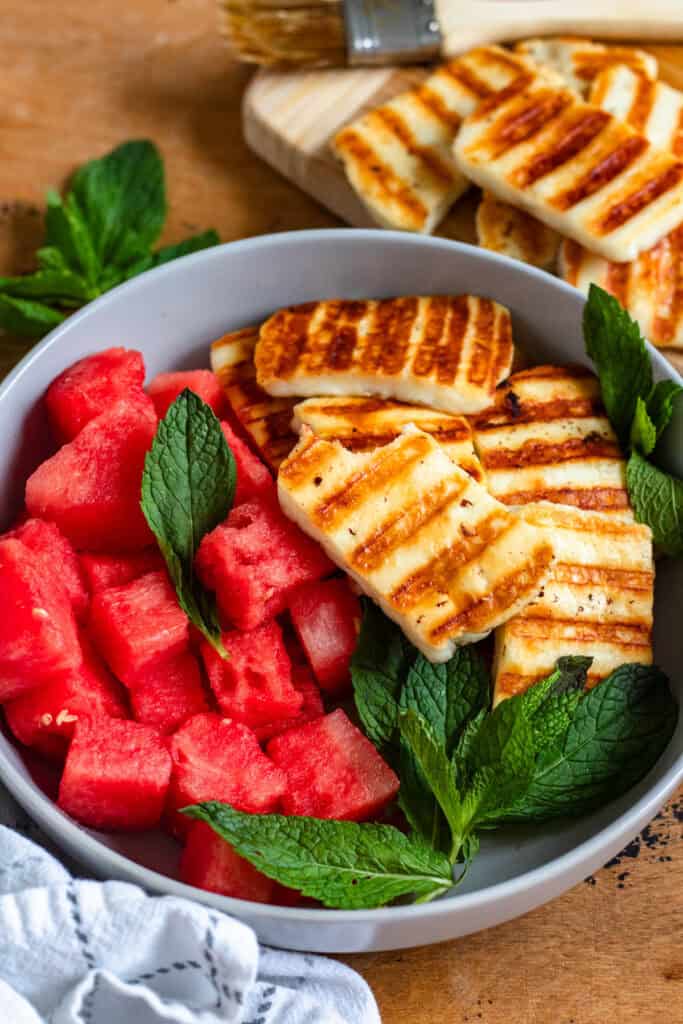 A vibrant bowl of grilled halloumi, juicy watermelon, and fresh mint leaves.