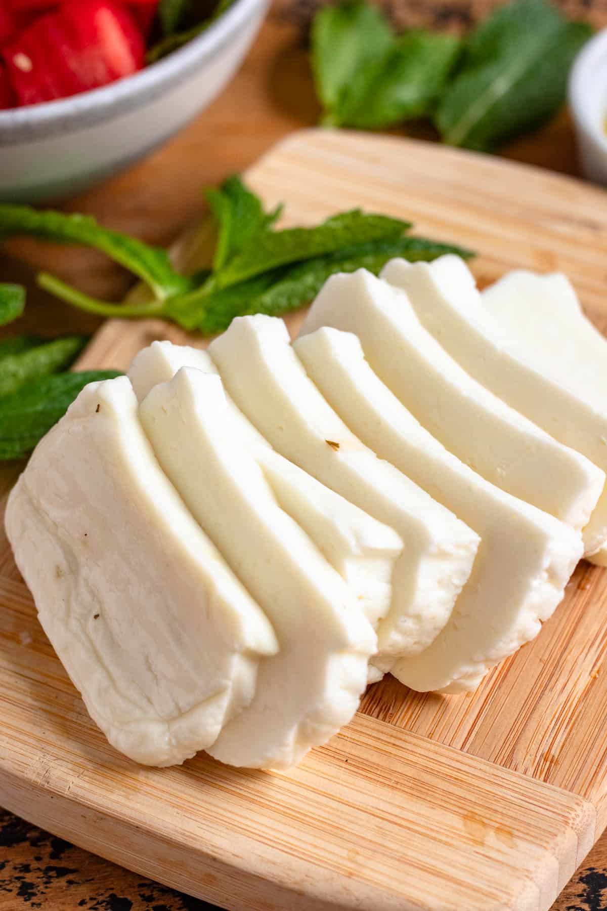 Sliced halloumi cheese on a wooden cutting board with fresh mint leaves in the background.