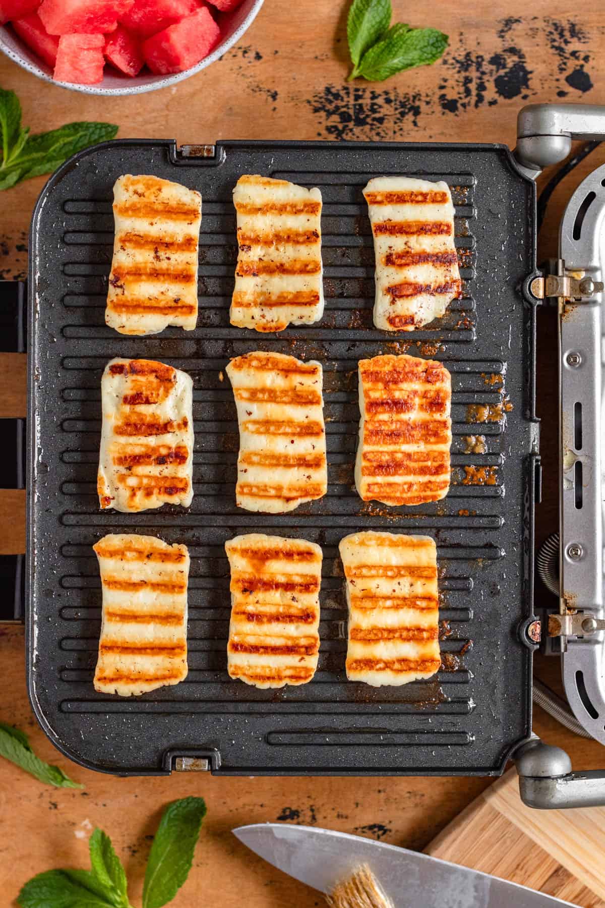 Slices of halloumi with golden grill marks sizzling on a hot griller.