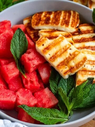 A vibrant bowl of grilled halloumi, juicy watermelon, and fresh mint leaves.