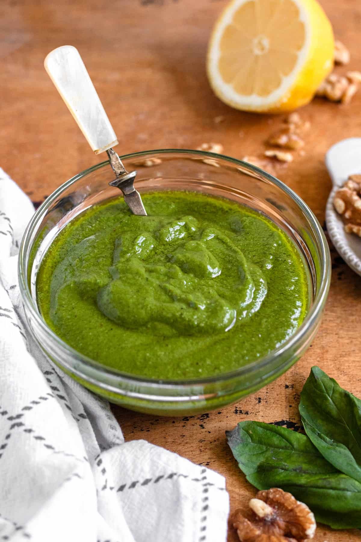 A bowl of walnut pesto with basil, lemon, and walnuts surrounding it.