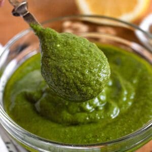 A spoonful of green walnut pesto in a glass bowl, with a halved lemon in the background.