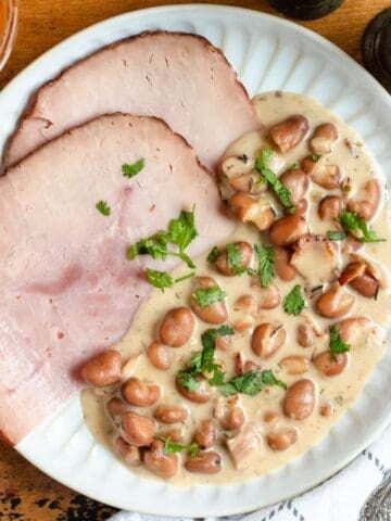 Creamy Judd mat Gaardebounen topped with fresh herbs on a white plate.