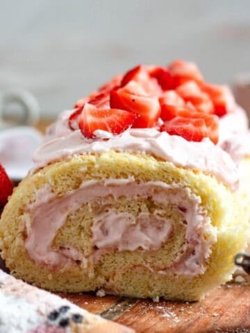 A light and fluffy strawberry Swiss roll topped with fresh strawberries sits on a wooden board.
