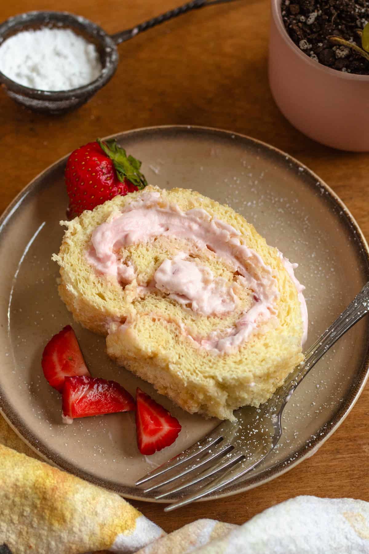 A slice of strawberry Swiss roll with fresh strawberry pieces on the side.