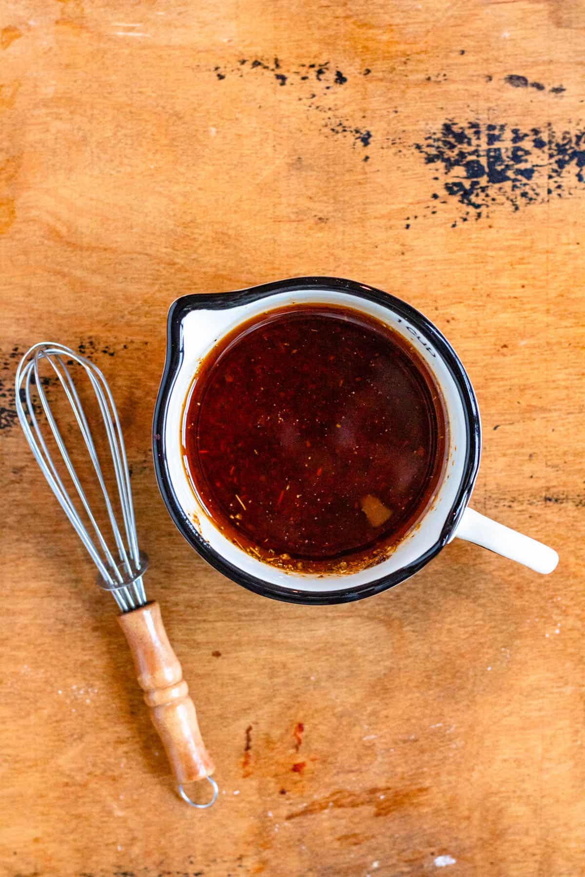 A cup of fajita sauce with a whisk by its side.
