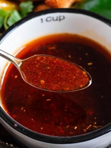 A cup of fajita sauce with a spoonful lifted above it.